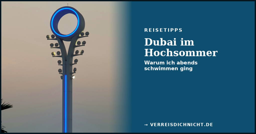 Beleuchteter Flutlichtmast mit blauem Leuchtring in Dubai bei Abenddämmerung, im Hintergrund das Meer, Textüberlagerung „Dubai im Hochsommer – Warum ich abends schwimmen ging"